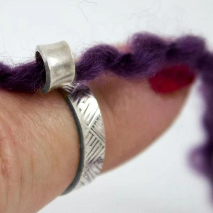 Ergonomic adjustable knitting ring, silver-toned metal, prevents yarn friction for comfortable crafting.