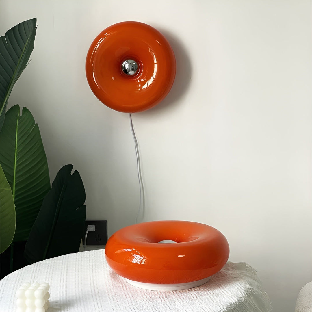 Orange donut-shaped LED lamp with warm glow, fits as a wall or table lamp, whimsical design with high-quality glass and metal