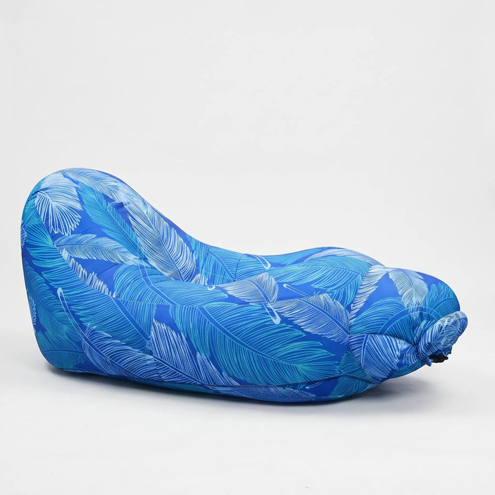 Blue inflatable outdoor lounge chair on a sandy beach, perfect for comfortable travel and sunbathing. Quick inflate.
