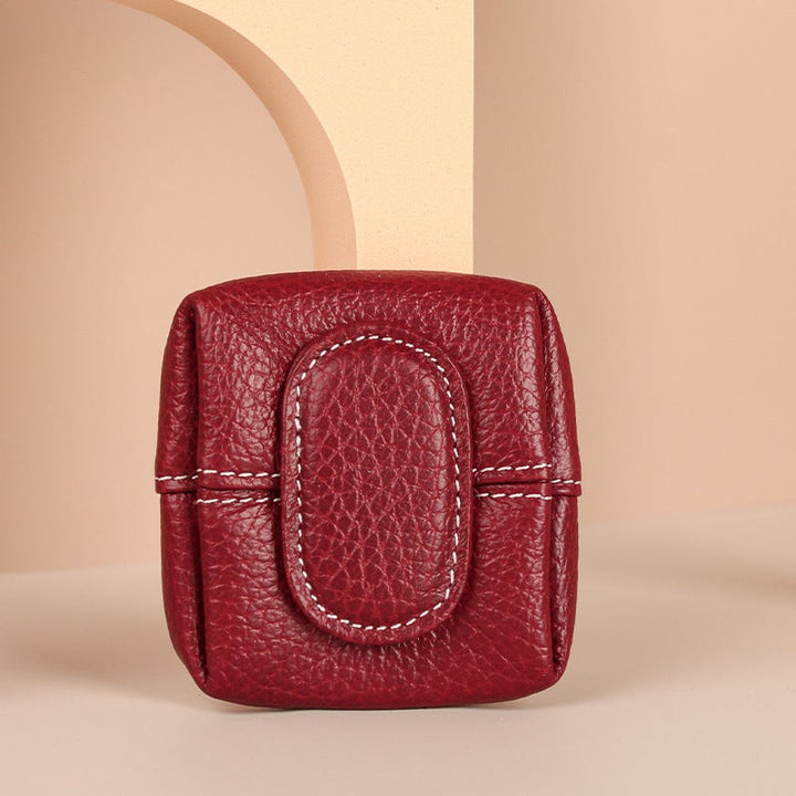 A hand placing a coin into a mini black leather coin purse, demonstrating use